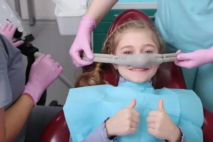 little girl giving thumbs up in dental chair, wearing mask for nitrous oxide, sedation dentistry Durham, NC family dentist
