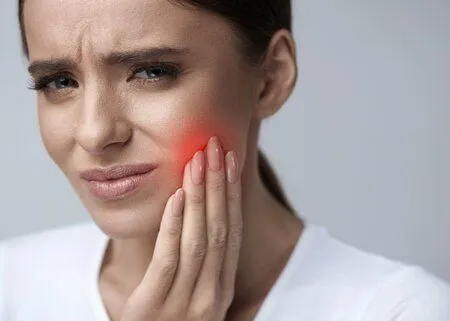 woman wincing and holding jaw in pain, red spot on face indicating pain, emergency dentistry Mt Airy, NC emergency dentist