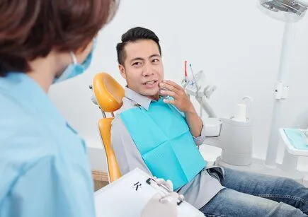 man gesturing to mouth in pain, sitting in dental exam chair looking up at female assistant, root canal treatment Oxnard, CA general dentistry