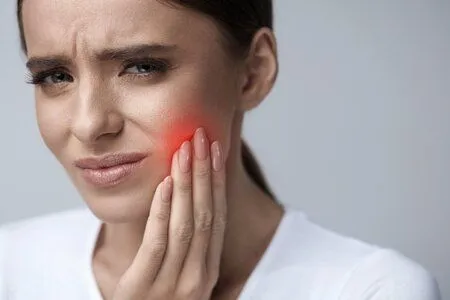 woman holding jaw and wincing, red area on face indicating dental pain, emergency dentist Old Bridge, NJ