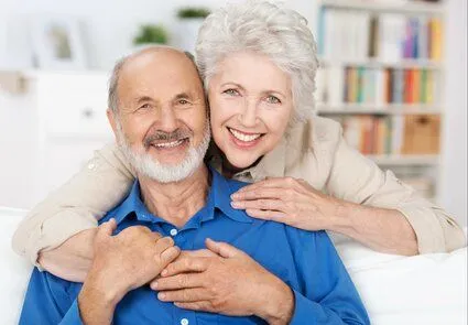 older woman smiling embracing older man sitting on couch, dentures Acton, MA general dentistry