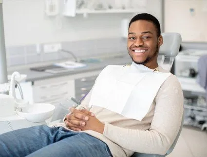 young black man smiling, sitting in dental exam chair wearing dental bib, general dentistry Katy, TX dentist
