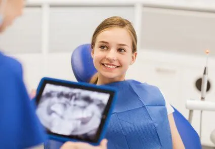 teen girl wearing dental bib in exam chair, dentist looking at digital x-ray, dentist Washington, DC oral surgery