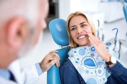 woman sitting in dental exam chair holding mouth in pain, needs root canal Pittsburgh, PA dentist