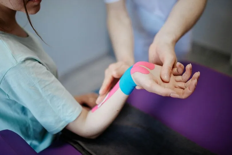 Doctor applying kinesiology tape to woman's wrist and forearm