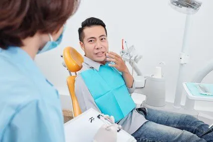 man sitting in dental exam chair gesturing to mouth in pain, needs root canal Hilo, HI