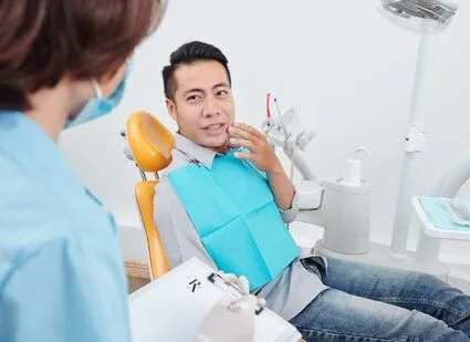 man sitting in dental exam chair gesturing to mouth in pain, talking to female dentist, root canals Old Bridge, NJ dentist 08857