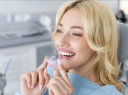 blond woman sitting in dental chair, placing clear aligners on top teeth, Invisalign Old Bridge, NJ dentist