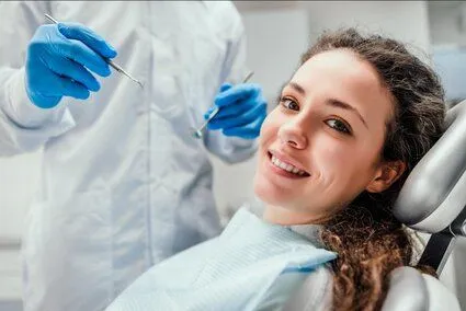 young woman smiling wearing dental bib, dentist in background, dental crowns Zebulon, NC dentist