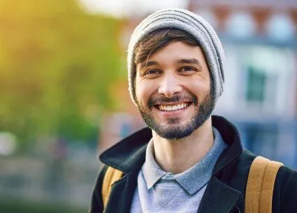 man outdoors wearing coat and winter hat, smiling nice teeth, implant dentistry Littleton, CO dentist