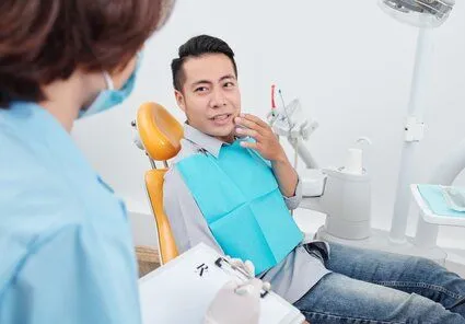 man gesturing to mouth in pain, sitting in dental exam chair looking up at female assistant, root canal Salem, OR dentist