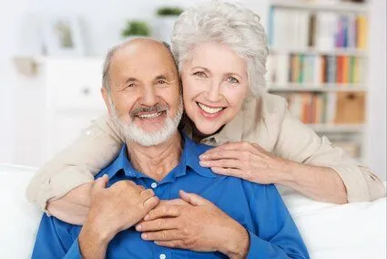 older man and woman smiling and hugging in living room, dentures Kanata, ON dentist