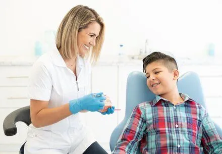 orthodontist showing model of teeth with braces to boy sitting in dental chair, orthodontics Katy, TX braces