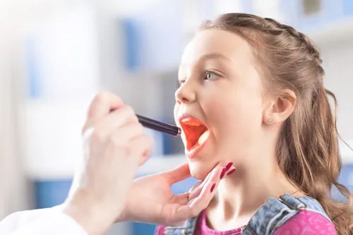 Child opening her mouth while pediatrician examines tonsils for tonsillitis symptoms