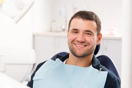 man wearing dental bib smiling, sitting in exam chair, laser dentistry Plantation, FL laser gum disease treatment
