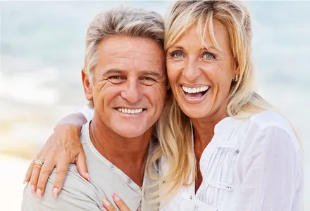 older man and woman smiling and embracing each other outside on beach, nice teeth with dentures Fond du Lac, WI dentist