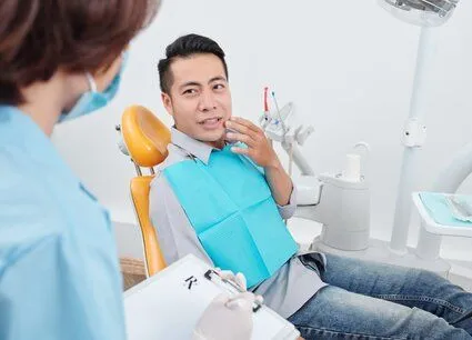 man sitting in dental exam chair gesturing to mouth in pain, talking to dentist needs root canal therapy New Baltimore, MI dentist