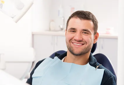 man wearing dental bib smiling, sitting in exam chair, general dentistry Reno, NV dental crowns