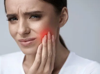 woman holding jaw in pain and wincing, red area on face to indicate pain area, emergency dental care Novi, MI dentist