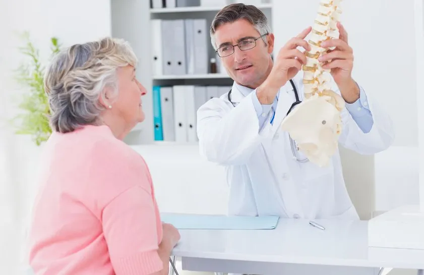 Chiropractor pointing to model spine with patient