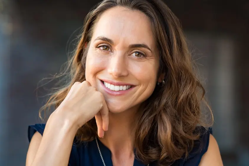 dark haired woman smiling, resting chin on her hand, nice teeth with veneers Niskayuna, NY dentist