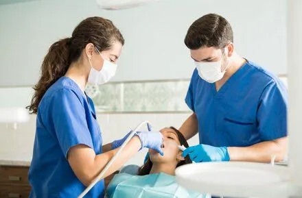 female dentist and male assistant do dental work on woman's teeth, dental fillings Naperville dentist