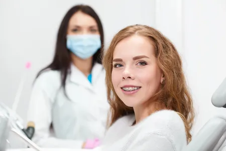 adult woman with braces sitting in exam chair, orthodontist in background, orthodontics for adults Milford, MI board certified orthodontist