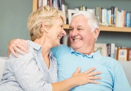 old couple smiling with dentures and sitting on couch, dentures Littleton, CO dentist 