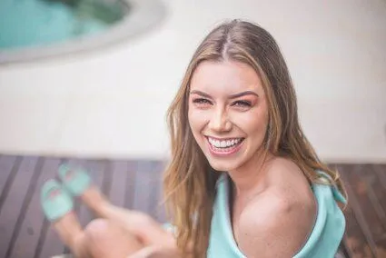 blond woman smiling nice teeth, sitting on deck near swimming pool, veneers Miramar, FL dentist