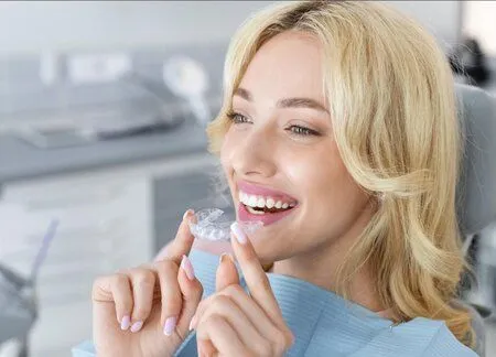 blond woman holding clear aligner tray, sitting in dental exam chair, Invisalign Plainfield, IL dentist