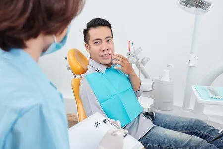 man sitting in dental exam chair, gesturing to mouth in pain talking to dentist, Durham, NC root canals
