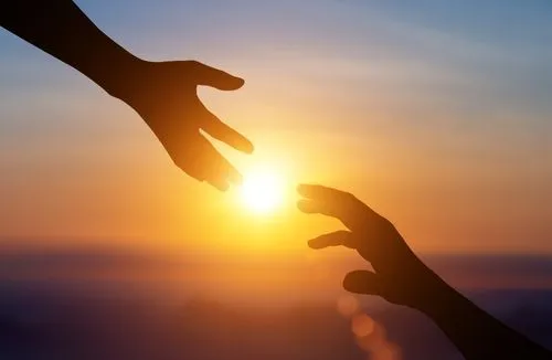 Hands reaching toward each other against a sunset sky, symbolizing healing and emotional connection in grief therapy.