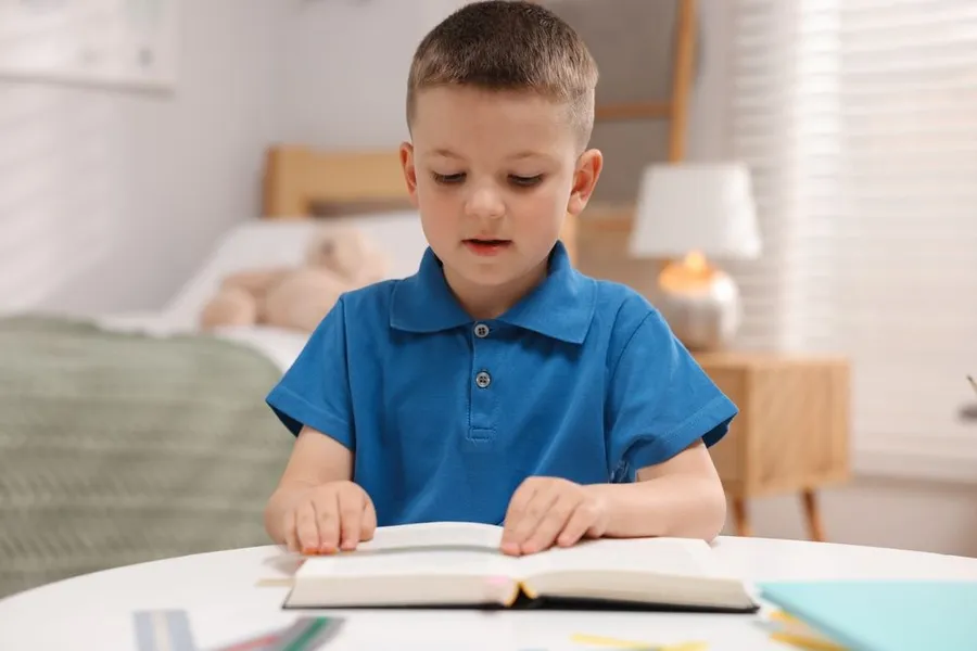 Little boy with Dyslexia reading book at table indoors