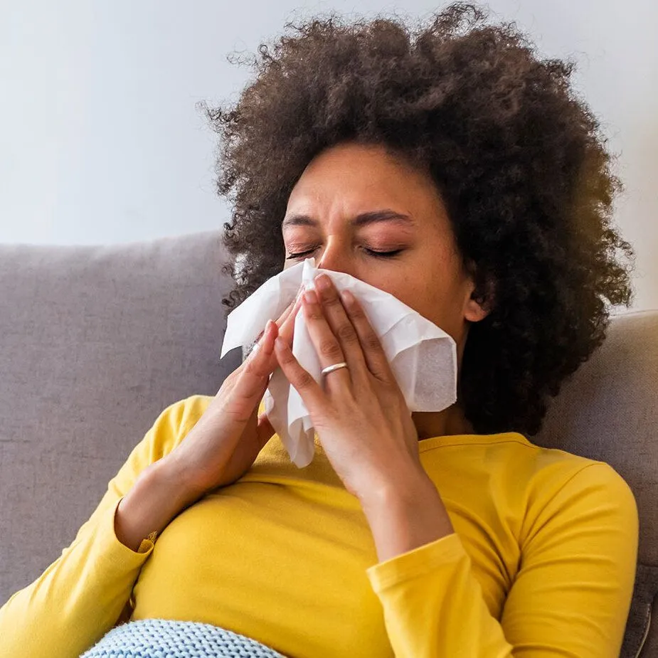 Woman with allergies blowing nose into tissue