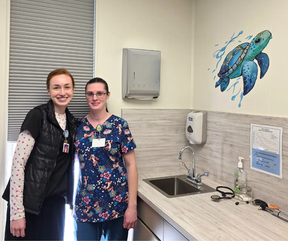 Two pediatric nurses standing next to sea creature mural in exam room