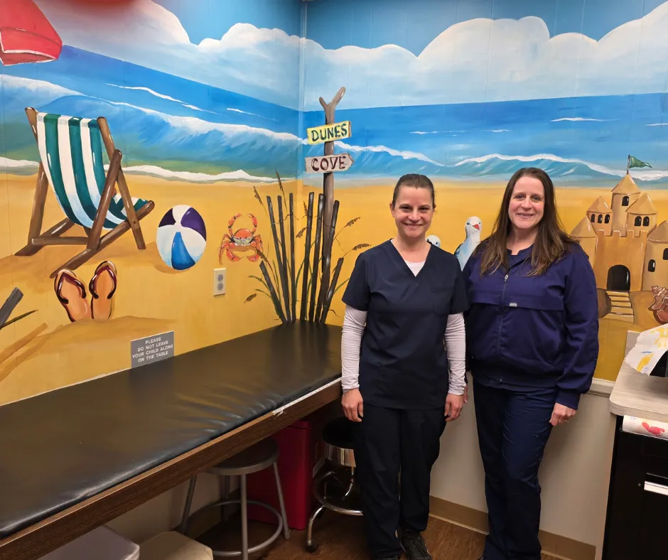 Two pediatric nurses standing next to beach mural in exam room