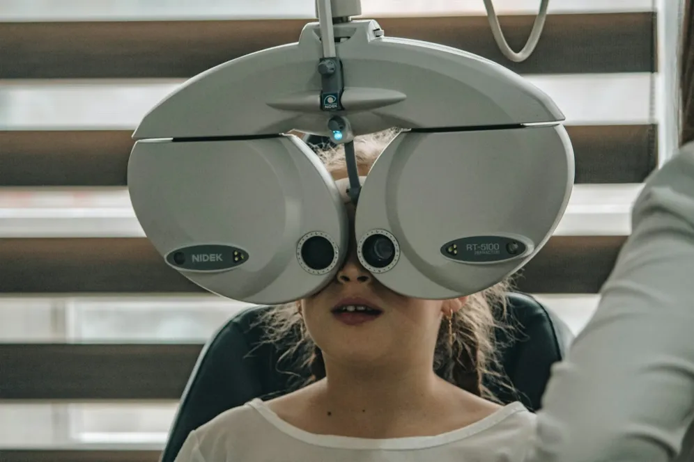 A girl sits behind an automated lens machine having her vision tested.